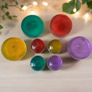 Een bovenaanzicht van vier handgemaakte, ronde Pure Color Tachyon oplaadschijven en koepels, gerangschikt van links naar rechts in de kleuren goudgeel, violetpaars, rood en turquoise, elk met een gladde, reflecterende afwerking.
